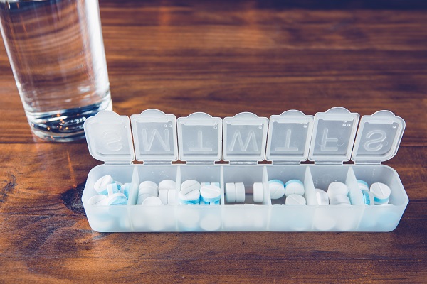 Tablets in an organiser on a table with a glass of water